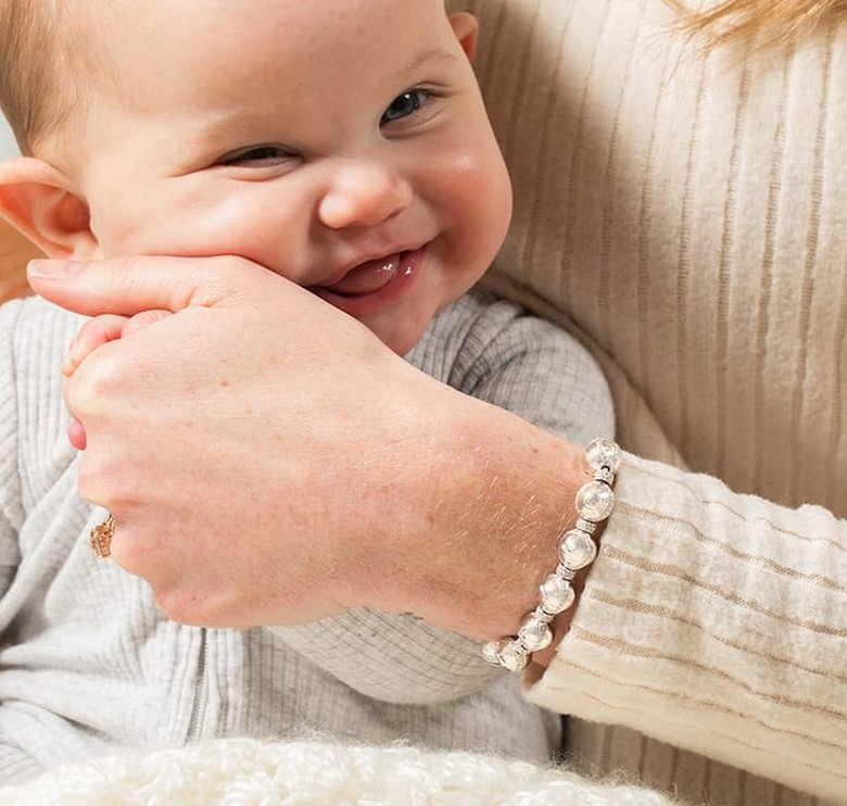 A mother holding her smiling baby, wearing a Charmed Beginnings pearl bracelet